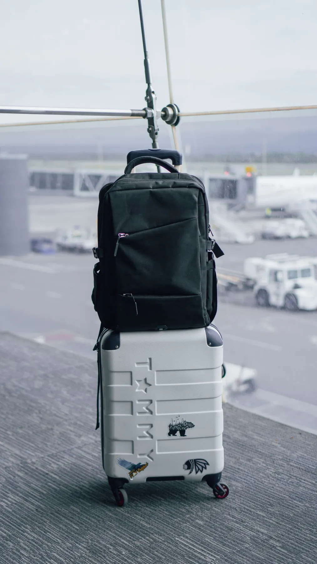 A black backpack on a wheeled suitcase inside an airport