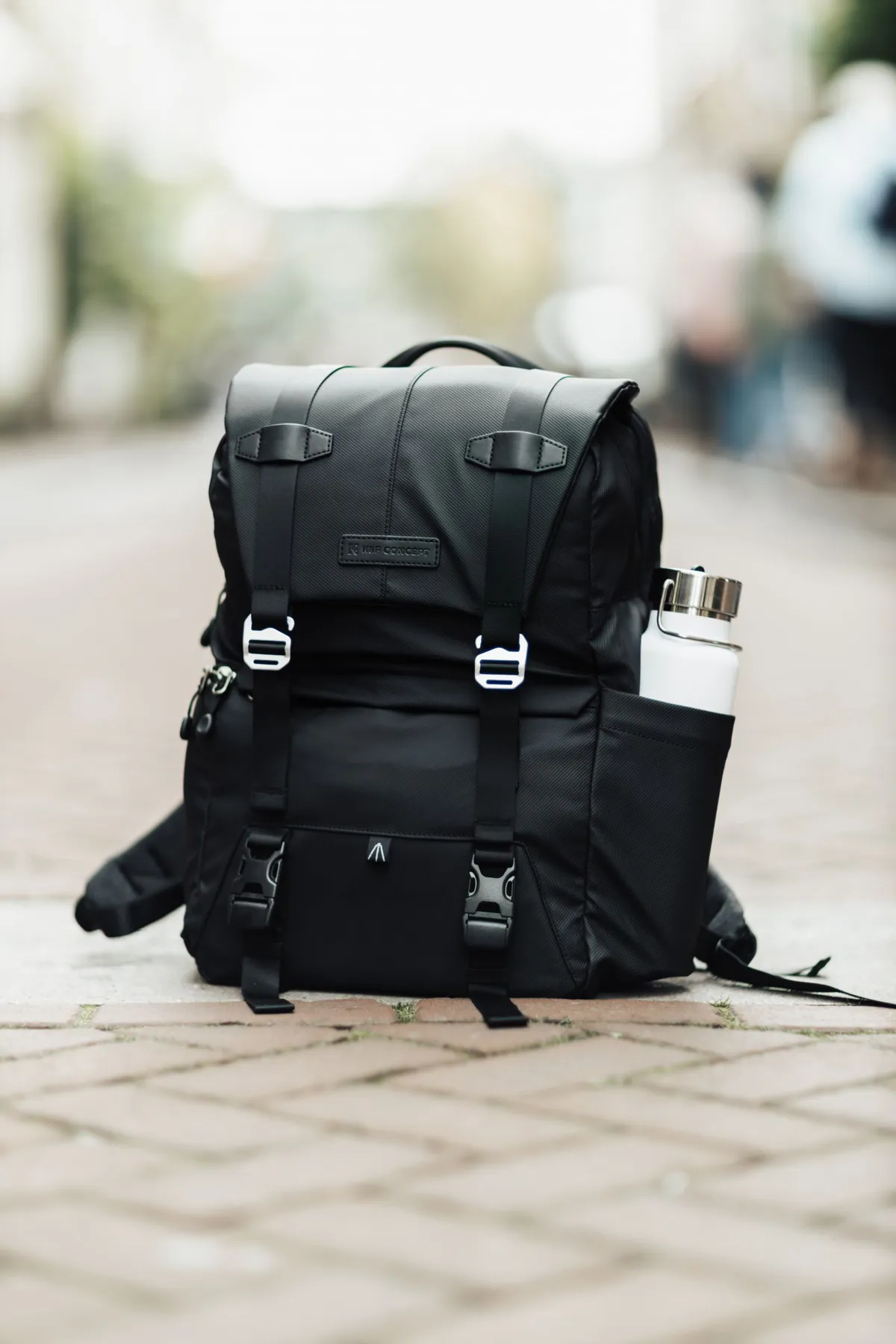 Black travel backpack with a bottle on a city sidewalk
